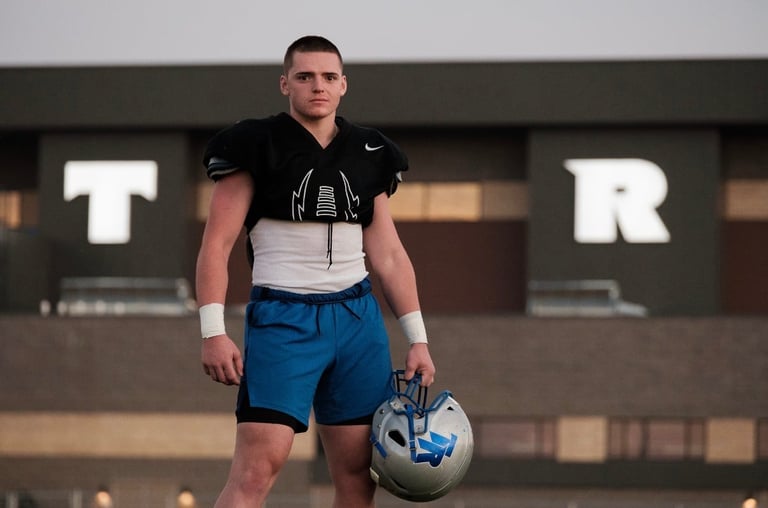 Young male athlete in football gear holding a helmet in front of stadium building